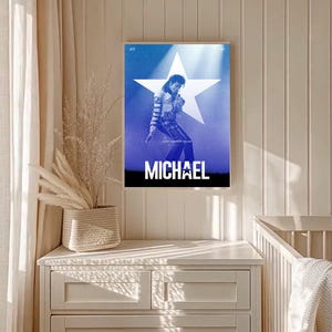 Könnte beinhalten: Gerahmtes Poster mit Michael Jackson in einer Performance-Pose vor blauem Hintergrund mit einem weißen Stern. Das Wort "MICHAEL" ist unten in Weiß gedruckt. Das Poster wird auf einer weißen Kommode präsentiert.