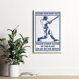 May include: A vintage-style baseball sign with a blue silhouette of a player swinging a bat. The sign reads "Players with short bats, Please stand closer to the plate or sit on the bench."