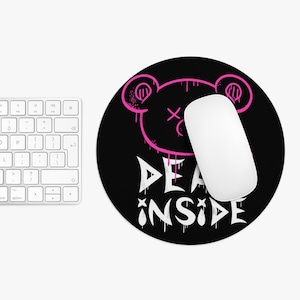 Puede incluir: Alfombrilla de ratón redonda negra con un diseño de oso rosa y las palabras "DEAD INSIDE" en blanco. Un ratón de ordenador blanco descansa sobre la alfombrilla. Un teclado blanco es parcialmente visible.