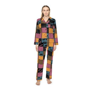 Pode incluir: Um conjunto de pijama de manga comprida com um padrão de patchwork de quadrados em tons de amarelo mostarda, rosa seco e azul-petróleo. O design inclui motivos pretos desenhados a linha, como espirais, pontos e traços. A parte superior tem gola com botões frontais e as calças a condizer têm um corte a direito.