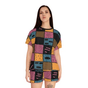 May include: A short-sleeve t-shirt and shorts set featuring a patchwork pattern of black, yellow, pink, and blue squares. The design includes various graphic elements such as spirals, cross-hatching, dots, and horizontal dashes across the fabric.