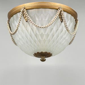 May include: An antique ceiling light fixture with a gold-toned metal rim and decorative chain accents. The frosted glass shade has a diamond pattern. The fixture has a decorative floral base and a small, round finial.