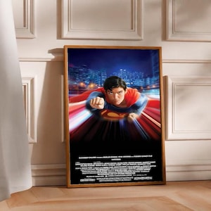 Può includere: Un poster incorniciato con Superman in volo, con un costume e un mantello rossi e blu. Lo sfondo mostra un paesaggio urbano notturno. Il poster ha una cornice in legno e include testo in basso.