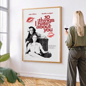 Könnte beinhalten: Gerahmtes Filmplakat für "10 Dinge, die ich an dir hasse" mit Julia Stiles und Heath Ledger. Das Poster zeigt einen roten Titel und Lippenstiftkussspuren. Eine Frau mit blonden Haaren hält ein Glas Rotwein.