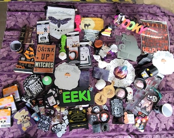 May include: A collection of Halloween-themed decorations and party supplies, including banners, signs, cups, and decorative items. The items feature spooky designs, such as bats, cats, skulls, and the text "Drink Up Witches" and "Eek!"