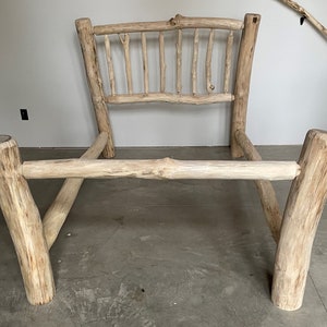 May include: A rustic wooden bed frame made from natural branches. The headboard and footboard are made from thick logs, and the rails are made from thinner branches. The frame is unfinished and has a natural wood color.