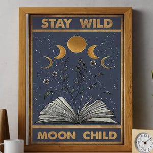 Könnte beinhalten: Ein Vintage-Poster mit blauem Hintergrund und goldener Schrift, auf dem "Stay Wild Moon Child" steht. Das Poster zeigt ein stilisiertes Bild eines offenen Buches, aus dem Blumen wachsen, umgeben von Monden und Sternen.