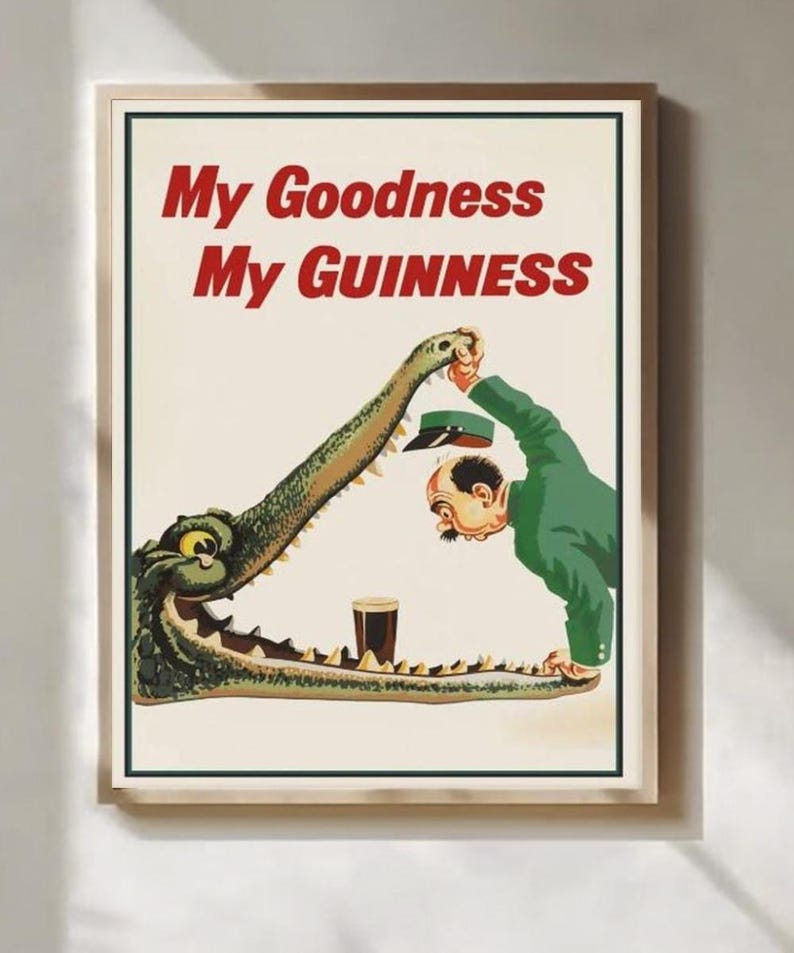 May include: Framed vintage advertisement with the text "My Goodness My Guinness." The image depicts a man in a green suit and a crocodile with a pint of Guinness in its mouth. The poster has a cream background.