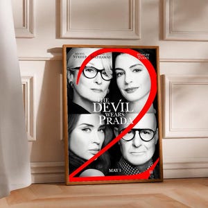 Könnte beinhalten: Ein gerahmtes Filmplakat für "Der Teufel trägt Prada" mit Meryl Streep, Anne Hathaway und Stanley Tucci. Eine große rote Zahl 2 ist über das Plakat gelegt. Das Plakat wird auf einem Holzboden präsentiert.