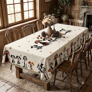 May include: A rectangular tablecloth featuring a repeating pattern of various dog breeds in black, white, and brown, accented with small paw prints and bone icons. The fabric is draped over a wooden dining table surrounded by matching wooden chairs.