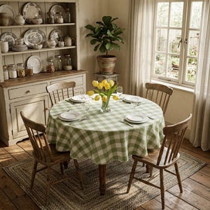 Peut inclure: Une table à manger ronde recouverte d'une nappe à carreaux vert sauge et blanc, dressée avec quatre assiettes et verres blancs. Quatre chaises en bois à barreaux entourent la table, agrémentée d'un vase en verre rempli de tulipes jaunes.