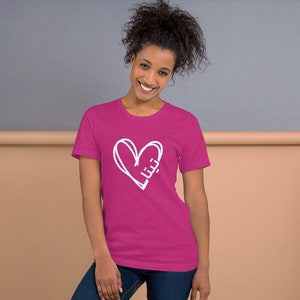 May include: A pink t-shirt with a white hand-drawn heart design. The heart is outlined in white and has a scribbled line through it.