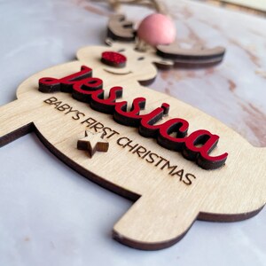 May include: A wooden reindeer ornament with the name "Jessica" and the text "Baby's First Christmas" in red lettering. A small star is also included on the ornament.