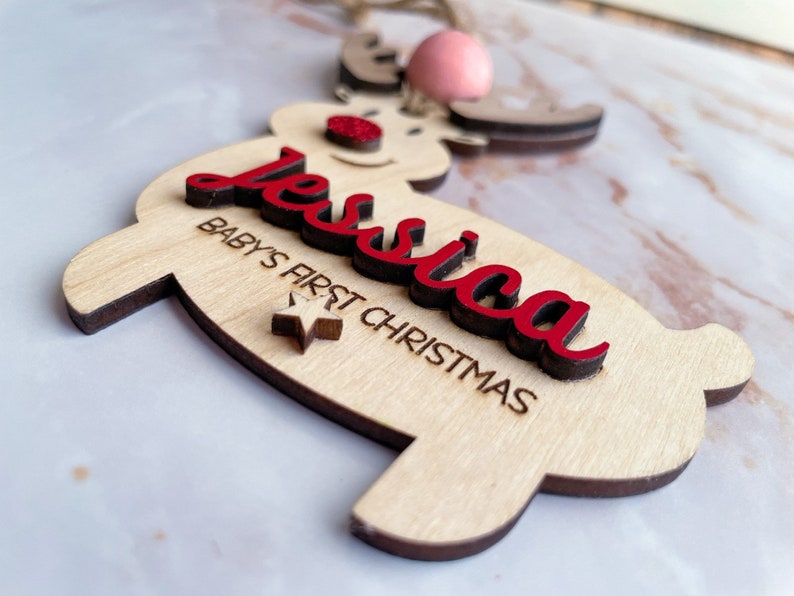 May include: A wooden reindeer ornament with the name "Jessica" and the text "Baby's First Christmas" in red lettering. A small star is also included on the ornament.