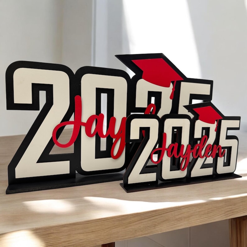May include: Black and white wooden cutout of the year 2025 with a red graduation cap and the name "Jayden" in red cursive lettering.