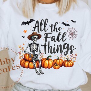 May include: White sweatshirt with a skeleton wearing a hat and holding a pumpkin. The text "All the Fall Things" is printed on the sweatshirt.