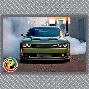 May include: A front view of a green Dodge Challenger SRT Hellcat car, with white headlights and smoke billowing from the tires. The car is parked on a brick road in an urban setting. The car has a black front bumper and a black hood.