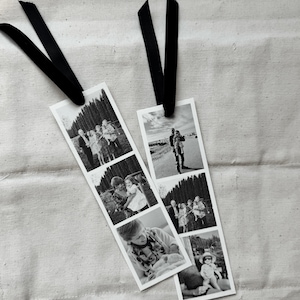 May include: Two black and white photo strip bookmarks with black ribbon attached. Each bookmark features a series of family photos. The bookmarks are laying on a white fabric surface.