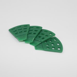May include: Four green, fan-shaped objects with a grid pattern are arranged on a white surface. The objects appear to be made of a solid material, possibly plastic or resin. The objects are evenly spaced and angled.