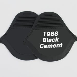 May include: Two black oven mitts with the text "1988 Black Cement" in white. The mitts have a unique shape with a textured top and stitched edges. The background is plain white.