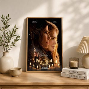 May include: A framed movie poster for Practical Magic 2 featuring the faces of two women in profile, the title text, and a scene of two figures standing among lit candles. The poster includes the names Sandra Bullock and Nicole Kidman at the top.