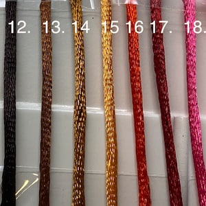May include: Close-up of 10 spools of embroidery floss in various colors, including beige, brown, gold, orange, red, pink, and purple. The spools are labeled with numbers 11 through 19.
