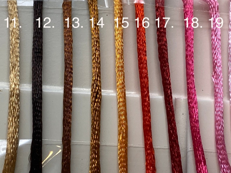 May include: Close-up of 10 spools of embroidery floss in various colors, including beige, brown, gold, orange, red, pink, and purple. The spools are labeled with numbers 11 through 19.