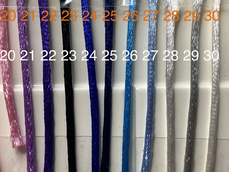 May include: A close-up of a selection of embroidery floss spools, numbered 20 through 30. The floss colors range from pink to light gray.