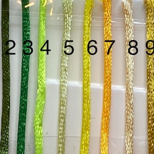 May include: Ten strands of embroidery floss in shades of green and yellow. The floss is numbered 1 through 10.