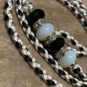 May include: A black and white braided cord with a beaded charm. The charm features black and white beads with rhinestones.