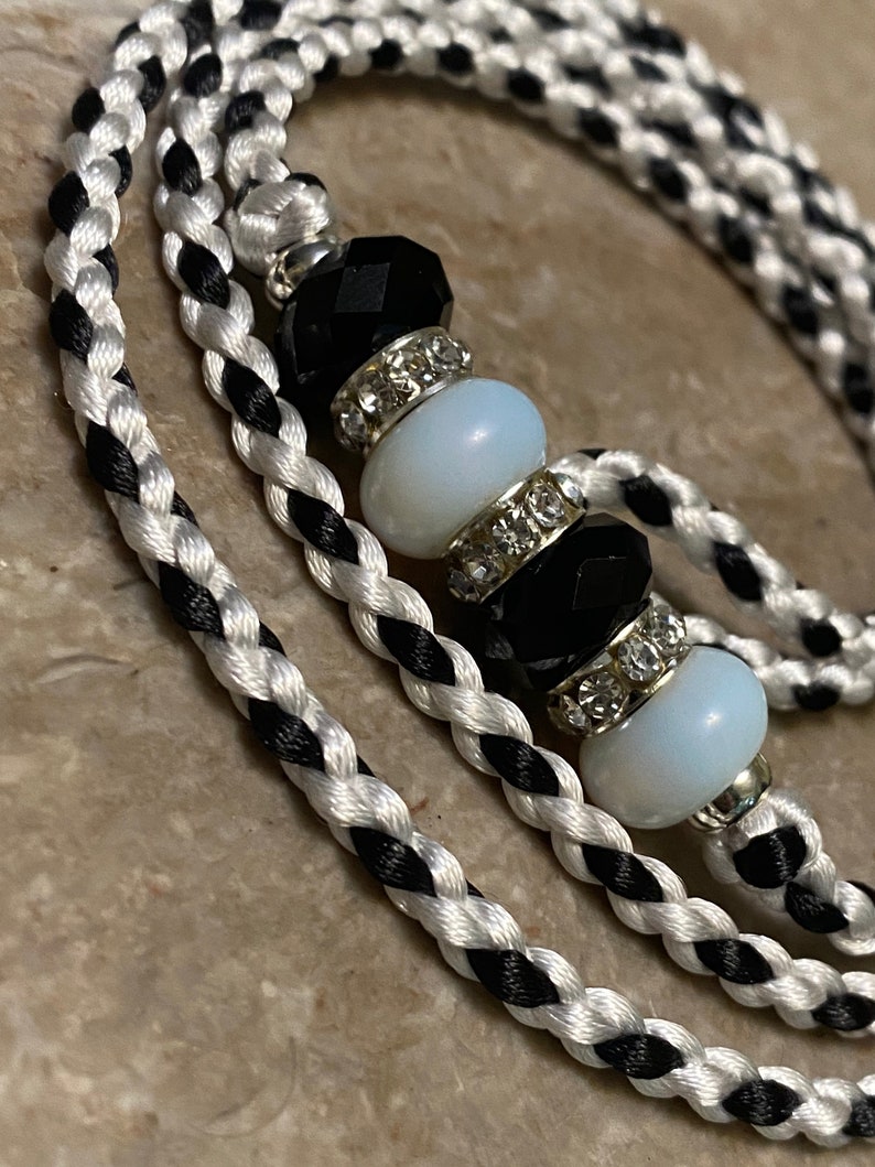 May include: A black and white braided cord with a beaded charm. The charm features black and white beads with rhinestones.