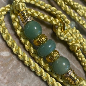 May include: A yellow braided rope leash with green and gold beads. The beads have a decorative design and some have small clear rhinestones.
