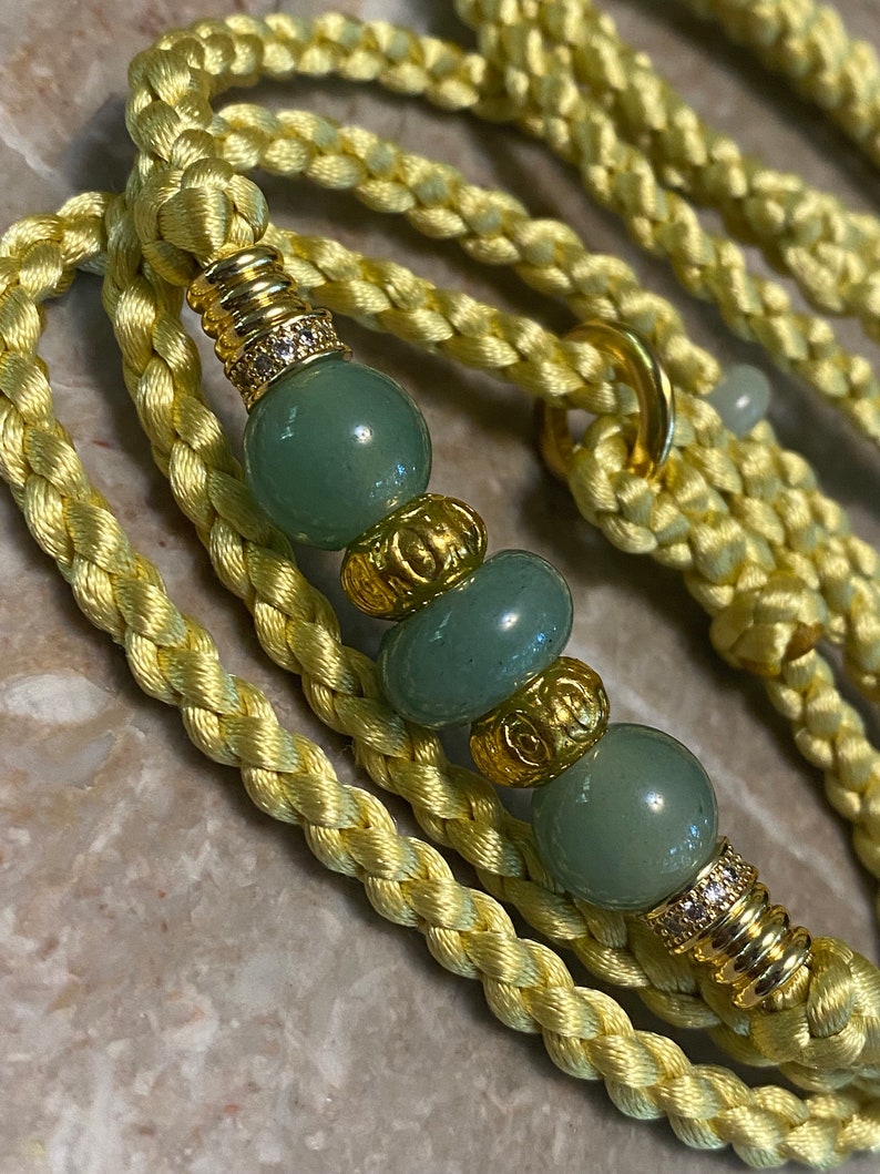 May include: A yellow braided rope leash with green and gold beads. The beads have a decorative design and some have small clear rhinestones.