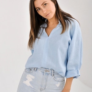 May include: A light blue linen shirt with a v-neck and long sleeves. The shirt is tucked into light blue distressed jeans.