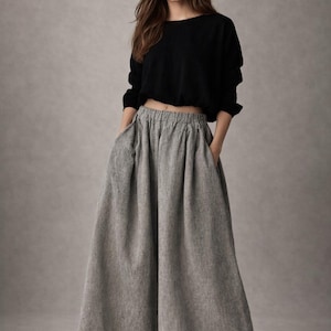 May include: A woman wearing a black long-sleeved crop top and wide-leg gray pants. The pants have pockets and a high waist. The outfit is casual and comfortable, suitable for everyday wear.