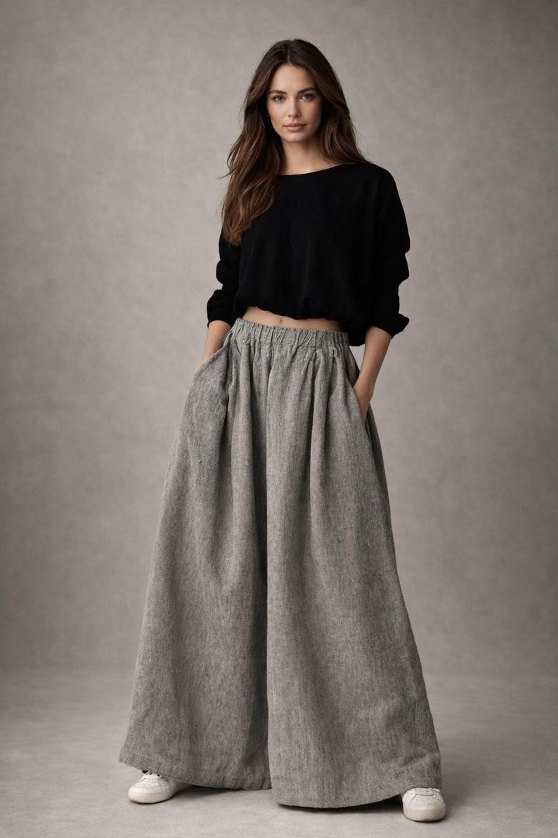 May include: A woman wearing a black long-sleeved crop top and wide-leg gray pants. The pants have pockets and a high waist. The outfit is casual and comfortable, suitable for everyday wear.