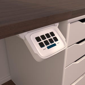 Könnte beinhalten: Ein weißes Tastenfeld mit einem blauen Bildschirm, das unter einer dunkelbraunen Arbeitsplatte montiert ist. Das Tastenfeld hat ein 3x4-Raster mit Tasten.