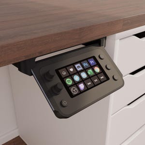 May include: A black control panel with a screen displaying icons for various apps, including social media, music streaming, and productivity software. The panel is mounted under a wooden desk.