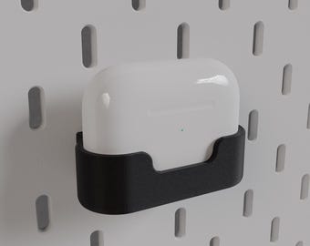 May include: A white wireless charging case with a black protective case, mounted on a white pegboard wall.
