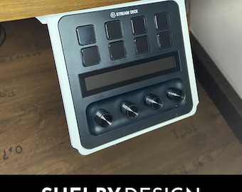 Puede incluir: Un panel de control Stream Deck negro con ocho botones cuadrados, una pantalla y cuatro perillas giratorias. El panel está montado debajo de una superficie de madera con un soporte blanco. El texto "STREAM DECK" es visible en la parte superior. El texto "SHELBY DESIGN" está en la parte inferior.