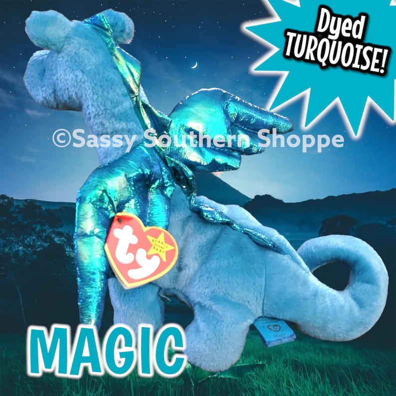 May include: A plush dragon toy with light blue fur and metallic turquoise wings. It features a heart-shaped red Ty tag attached to the chest and a blue tag on the tail. The text "Dyed TURQUOISE!" and "MAGIC" are visible, along with "Sassy Southern Shoppe".