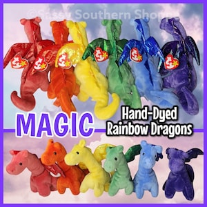 May include: A collection of hand-dyed rainbow dragon plush toys in various colors, including red, orange, yellow, green, blue, and purple. Each dragon has a tag attached. The word "MAGIC" is displayed in large, purple letters.