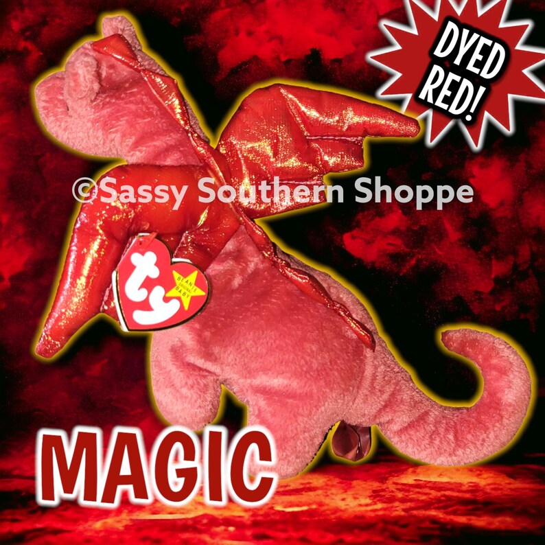 May include: A red plush dragon toy with shiny red wings and a heart-shaped Ty tag attached to its neck. The toy features the text MAGIC at the bottom, Sassy Southern Shoppe in the centre, and a starburst graphic with the text DYED RED!