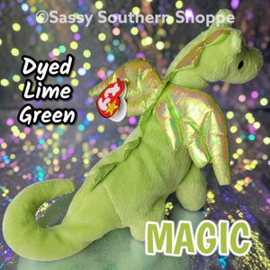 May include: A lime green plush dragon toy with iridescent wings and a red heart-shaped tag attached to its neck. The text Dyed Lime Green and MAGIC are visible on the image, along with the copyright text Sassy Southern Shoppe.