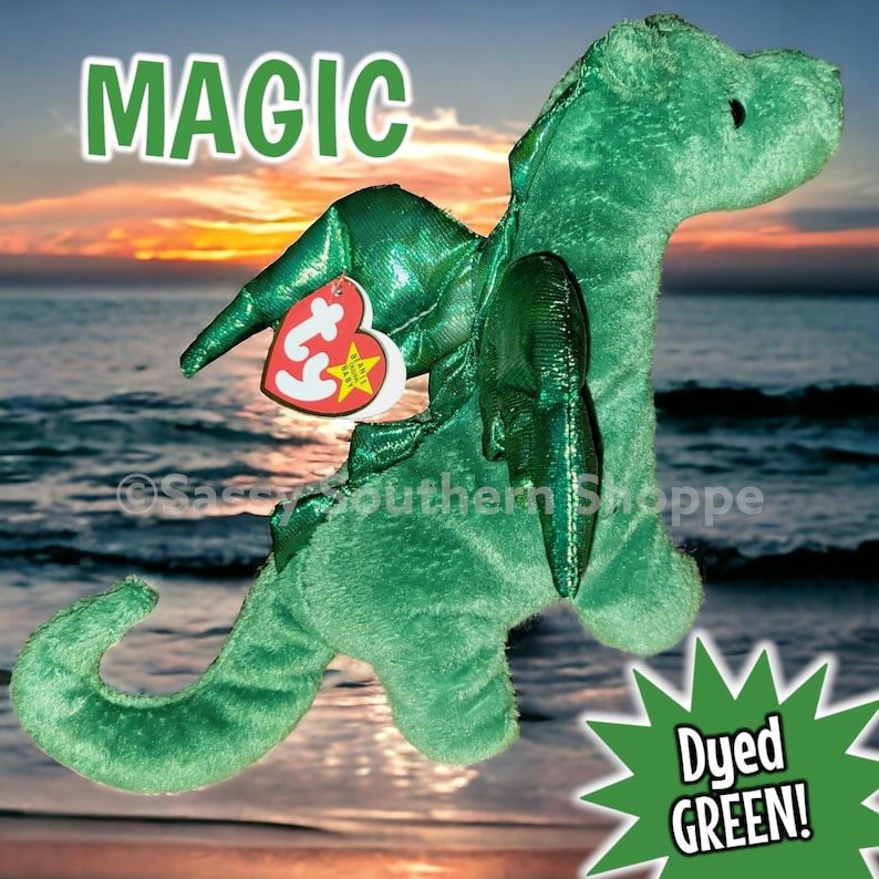 May include: A green plush dragon toy with a textured surface, featuring a heart-shaped red and white Ty Beanie Baby tag attached to its wing. The word MAGIC is printed in green at the top, and a green starburst graphic says Dyed GREEN!