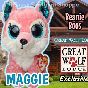 May include: A pink plush Maggie Beanie Boo wolf with large blue glitter eyes and teal glitter ears. The plush toy has a Ty heart tag. The image includes the text "Great Wolf Lodge Exclusive".