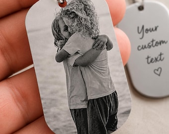 Puede incluir: Un llavero de placa de metal plateado con una fotografía grabada en blanco y negro de dos niños abrazándose. Una segunda placa a juego en el fondo muestra el texto grabado Your custom text y el símbolo de un pequeño corazón.