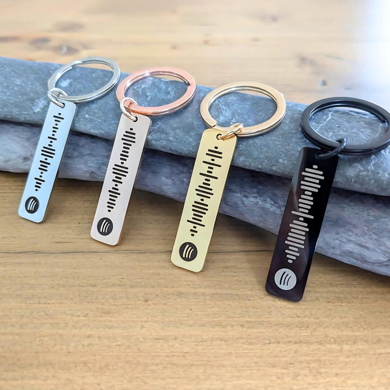 以下が含まれることがあります： 異なる色の金属タグが付いた4つのキーホルダー。各タグには白黒のバーコードと小さなロゴがあります。キーホルダーはシルバー、ゴールド、ローズゴールド、ブラックです。
