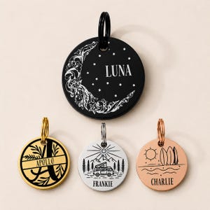 May include: A collection of four round pet tags. One black tag features a crescent moon design and the name "LUNA." Other tags are gold, silver, and rose gold, each with unique designs and pet names: "APOLLO," "FRANKIE," and "CHARLIE."
