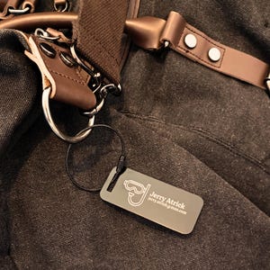 Könnte beinhalten: Ein silbernes Metalletikett für Gepäck mit einem Tauchmasken-Symbol und dem Text "Jerry Atrick" und "jerry.atrick@mail.com".